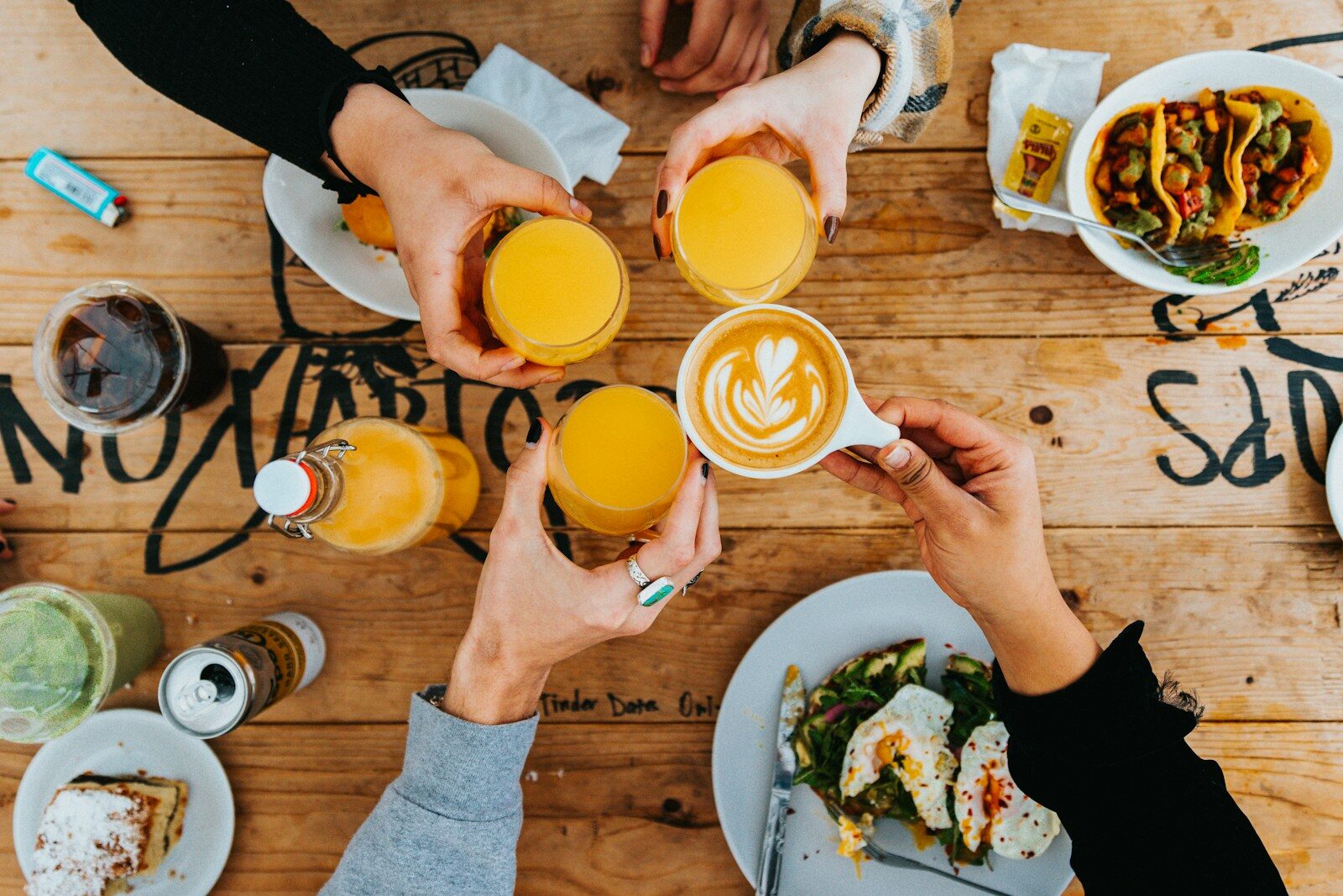 Cheers with colorful drinks at a table filled with food, highlighting a social gathering and brunch atmosphere.